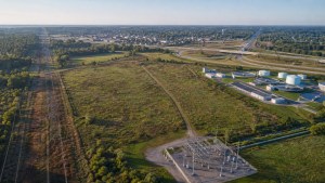 Aerial view of an undeveloped parcel near transmission lines, a substation, highway access, municipal water infrastructure, and a neighboring community.